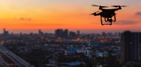 Silhouette of drone flying above city at sunset