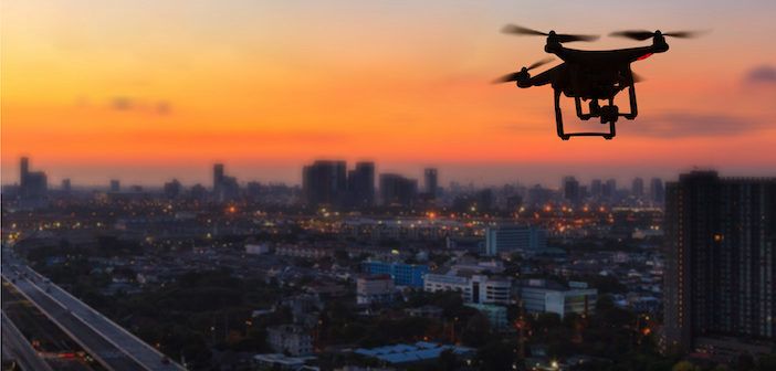 Silhouette of drone flying above city at sunset