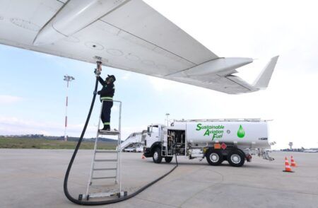 A worker refuels an aircraft with sustainable aviation fuel from a tanker truck on an airport tarmac