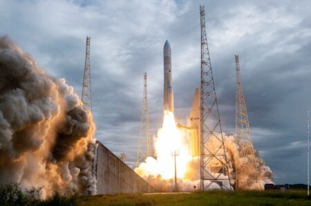 A powerful rocket launches vertically into a cloudy sky, surrounded by tall metal structures and billowing smoke at its base. The scene captures the dynamic energy of the lift-off, with the rocket's bright flames contrasting against the ominous clouds