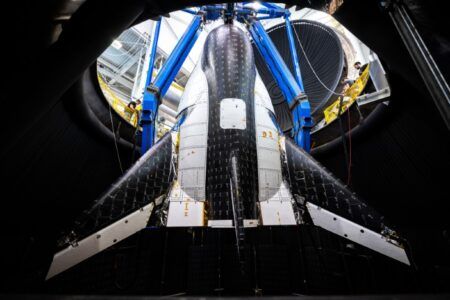 Bottom-up view of Dream Chaser showing detailed thermal protection tile pattern and wing structure with technicians working on overhead lifting fixture