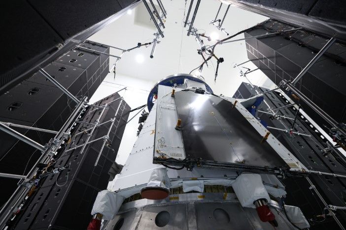 View from below as Dream Chaser spacecraft is positioned inside structural test chamber, showing underside access panels and test integration hardware