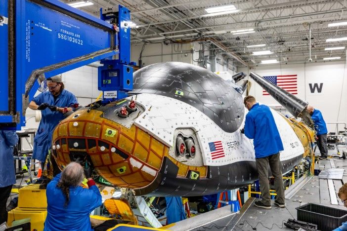 Dream Chaser spaceplane undergoing structural testing with technicians working on its thermal protection system and structural components inside a test facility