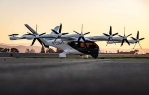 White electric aircraft with multiple propellers on tarmac during sunset