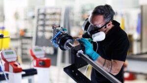 Manufacturing worker wearing protective mask and gloves working on blue and black aerospace component in factory setting