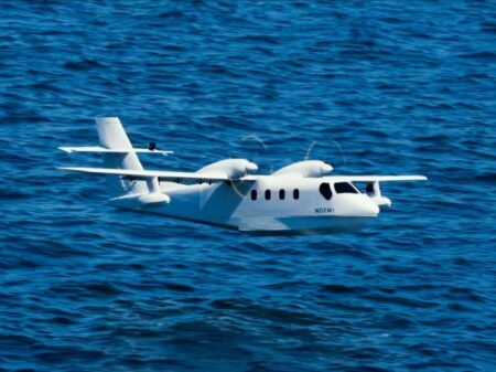 White twin-engine seaplane with high-wing configuration and twin floats on water surface showing Noemi branding on fuselage