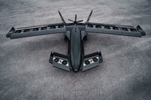 Gray military-style aircraft with tilting wing configuration and multiple propellers on tarmac