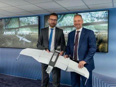 Two executives in business suits holding unmanned aircraft model in front of Airbus display screens