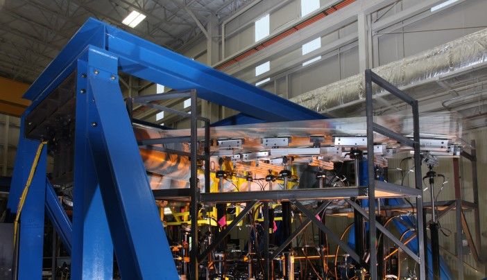 Aircraft structural component secured in blue testing frame with monitoring equipment in industrial laboratory setting