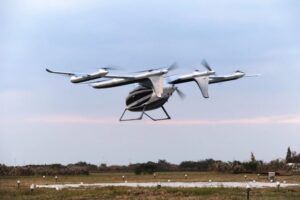 White eVTOL aircraft with multiple rotors in flight over rural landscape