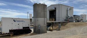 Industrial facility showing cylindrical test stand structure with support equipment and Frontier Aerospace trailer