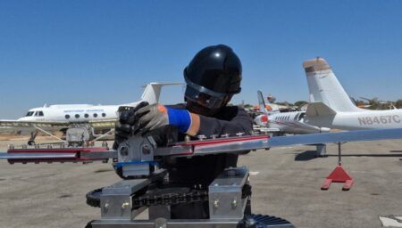 Technician in black helmet operating Hydroplane's hydrogen fuel cell powered rotor test stand on airport tarmac with aircraft in background