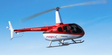 Red and white Robinson R44 helicopter in flight against blue sky with magniX and Robinson branding visible on fuselage] Caption: magniX previously powered the first flight of a retrofitted electric Robinson R44 helicopter in 2022 (Image: magniX) Description: The partnership builds on magniX's previous success with electric helicopter conversions including the world's first piloted hydrogen-electric helicopter flight