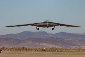B-21 Raider stealth bomber in flight above desert terrain with mountains in background