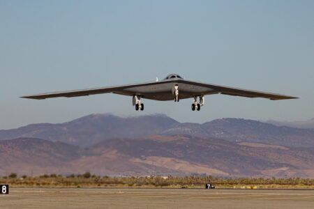B-21 Raider stealth bomber in flight above desert terrain with mountains in background