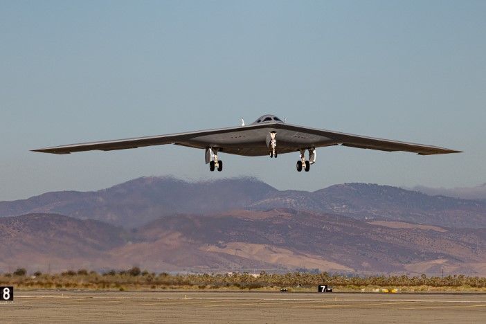 B-21 Raider stealth bomber in flight above desert terrain with mountains in background