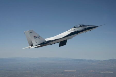 NASA F-15 research jet in flight over the California desert with the CATNLF scale-model wing mounted vertically beneath the fuselage