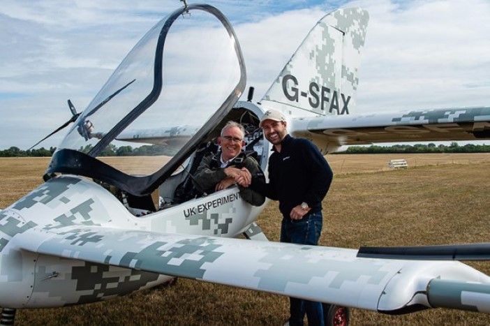 Two men shaking hands beside a SkyFly Axe eVTOL on a grass airstrip