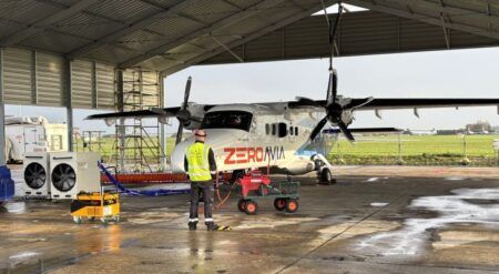 ZeroAvia-branded Dornier 228 aircraft parked under a shelter at the company's liquid hydrogen test facility, with a technician and ground support equipment in the foreground
