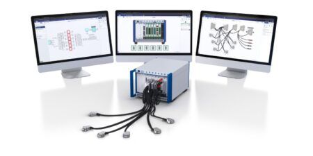 Three monitors displaying Test System Architect software interfaces alongside a PXI chassis with connected cables