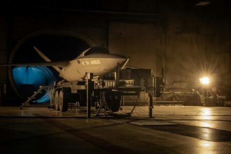 A Kratos Valkyrie uncrewed combat aircraft bearing Airbus markings on a ground support cradle inside a hangar facility