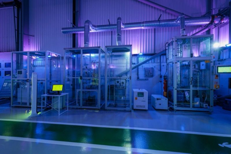 Glass-walled process units inside the Sustainability Innovation Centre, with control monitors and aluminum framing visible under purple and blue interior lighting