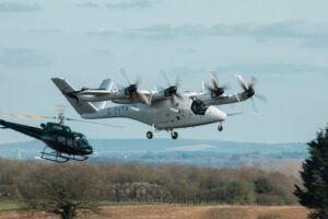 Vertical Aerospace eVTOL aircraft in flight during transition testing at Cotswold Airport with a chase helicopter visible in the background