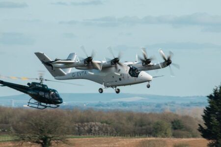 Vertical Aerospace eVTOL aircraft in flight during transition testing at Cotswold Airport with a chase helicopter visible in the background