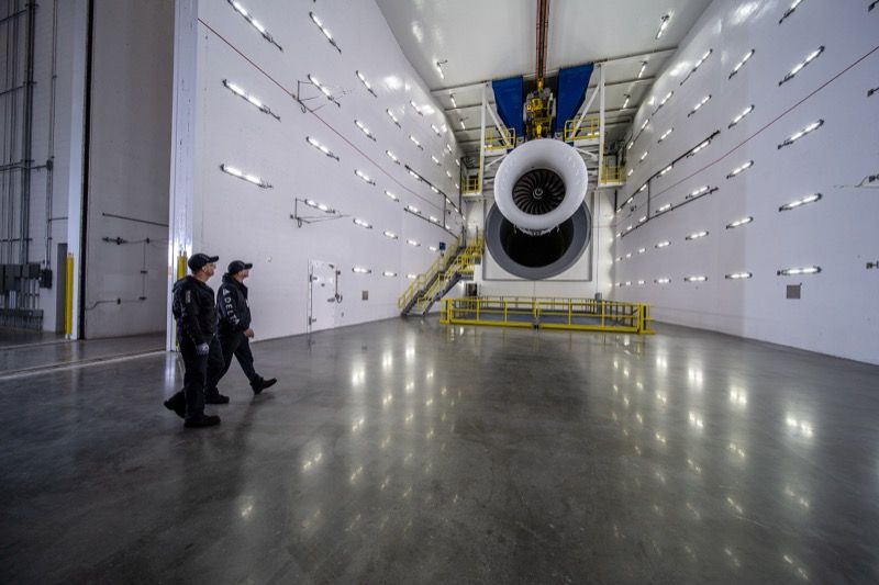 Two Delta TechOps technicians walking across the polished floor of Test Cell 5 toward a large turbofan engine mounted on a test stand