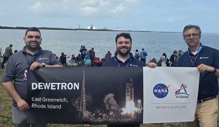 Three members of the Dewetron US team hold a company banner and a NASA Artemis supplier banner at Kennedy Space Center on launch day