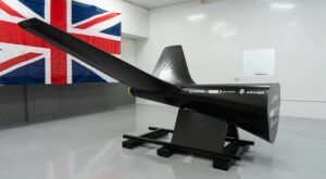 Aft fuselage and tail section of a black autonomous platform demonstrator bearing Anduril, GKN Aerospace and Archer logos, mounted on a test stand in front of a Union Jack flag