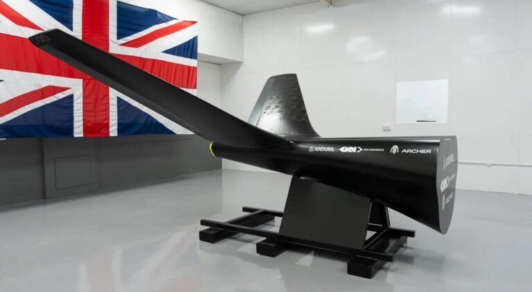 Aft fuselage and tail section of a black autonomous platform demonstrator bearing Anduril, GKN Aerospace and Archer logos, mounted on a test stand in front of a Union Jack flag