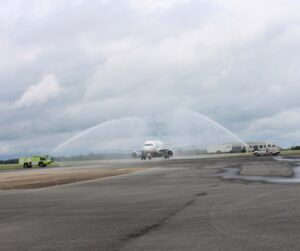 An Airbus A319 taxiing under a water cannon salute from two fire trucks on an airport apron
