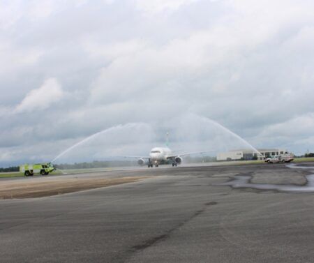 An Airbus A319 taxiing under a water cannon salute from two fire trucks on an airport apron
