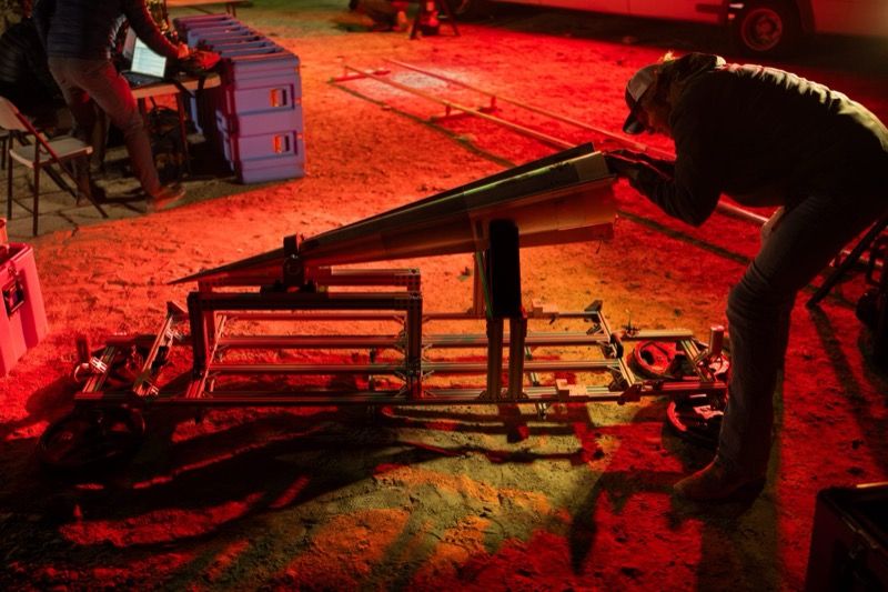 A researcher works on a cone-shaped flight test vehicle mounted on a metal frame under red lighting at night