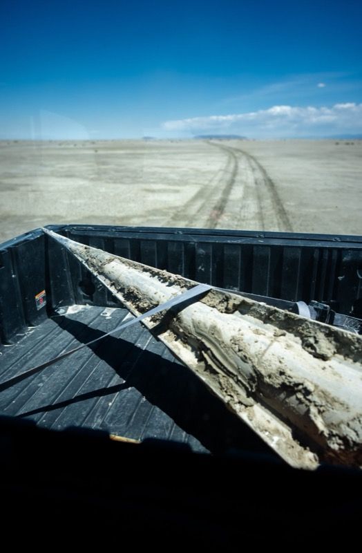 A mud-covered cone-shaped vehicle section lies in the bed of a pickup truck on a desert track