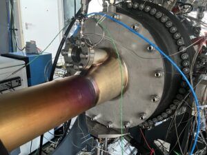 Hydrogen sector combustor test rig at DLR Institute of Space Propulsion, Lampoldshausen, showing heat-discolored fuel inlet pipe connected to a circular test chamber flanked by instrumentation cabling