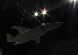 A grey MQ-28 Ghost Bat aircraft model suspended by wires inside a darkened radar test chamber lined with anechoic absorber material