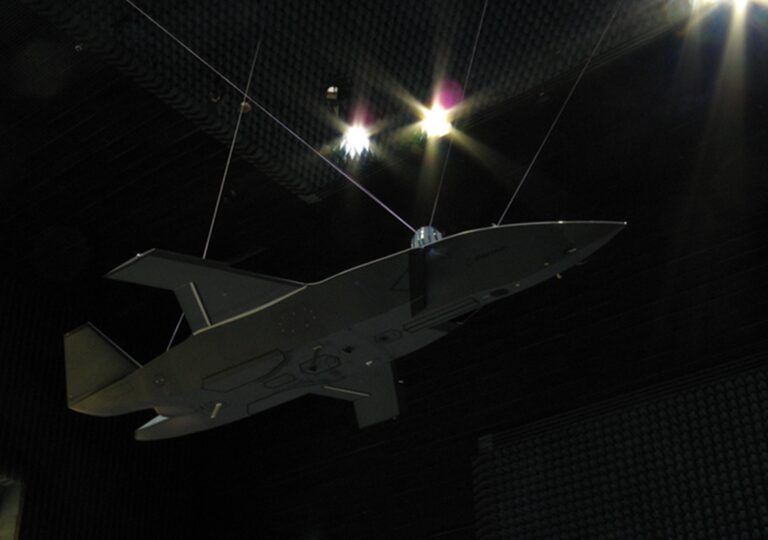 A grey MQ-28 Ghost Bat aircraft model suspended by wires inside a darkened radar test chamber lined with anechoic absorber material