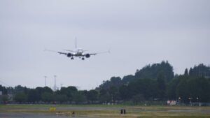 A Boeing 737-10 test aircraft on final approach to land at Boeing Field on an overcast day, with landing gear extended over the airfield perimeter