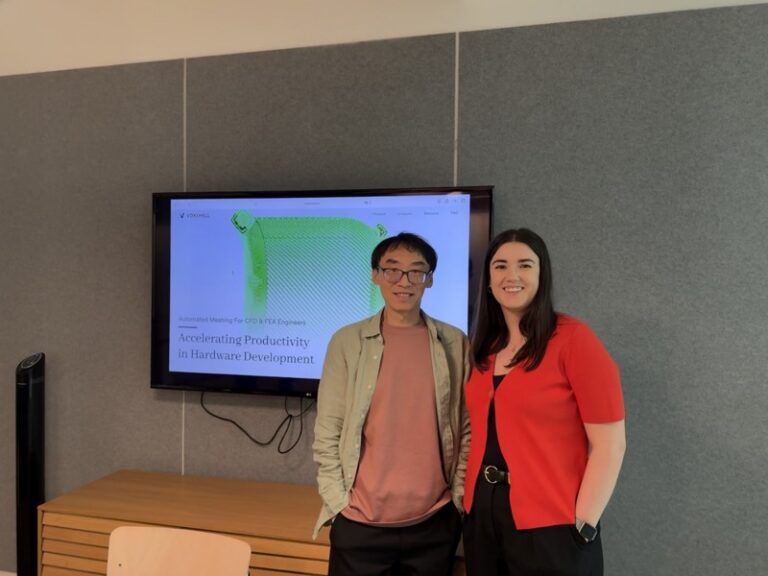 Two people standing in front of a screen displaying the Voxshell website and a mesh model of an engineering component