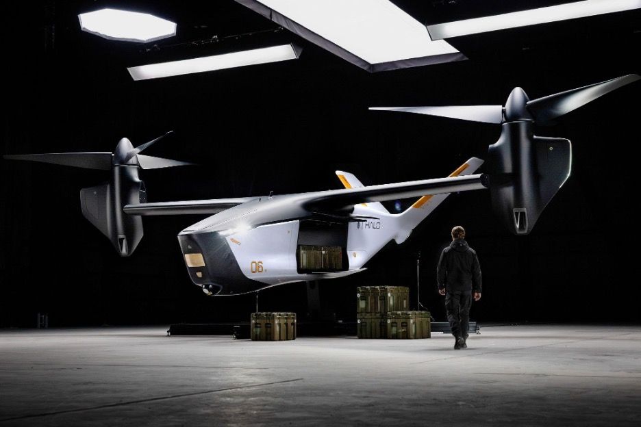 Archer’s Halo autonomous tiltrotor aircraft in a darkened hangar beside modular cargo containers, with a person walking towards it for scale