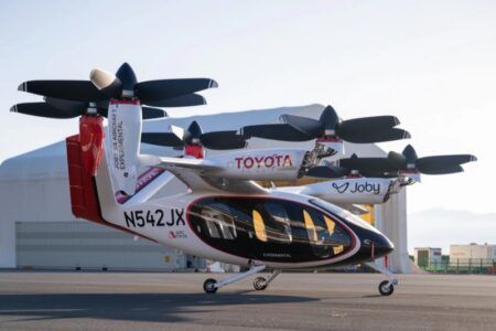 Alt text: Joby S4 aircraft displaying Toyota and Joby branding parked on an airfield apron with its rotors raised