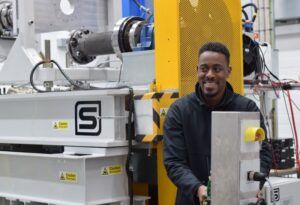 An engineer standing beside white and yellow transmission test rig equipment in a laboratory at Hewland’s Technical Centre