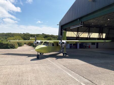 Britten-Norman begins testing first fully UK-built Islander A lime-green twin-propeller Britten-Norman Islander parked on tarmac outside a hangar under clear skies