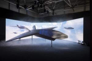 The Brontanax prototype on a stand during its unveiling, in front of a curved screen showing computer-generated aircraft flying through cloud