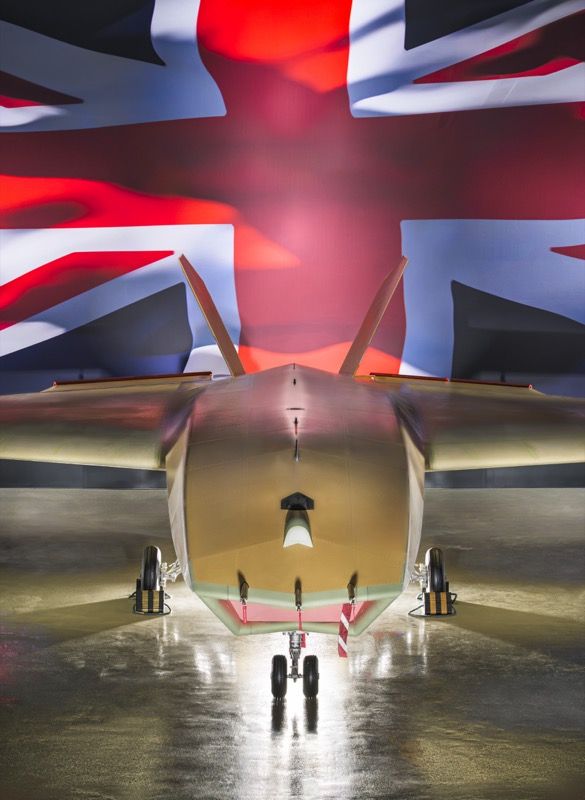 Front view of the Brontanax uncrewed combat aircraft in a hangar, landing gear down with remove-before-flight tags, against a large Union flag backdrop