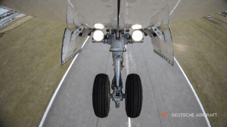Deutsche Aircraft completes first flights of landing gear testbed View from beneath a D328 aircraft looking at its extended twin-wheel nose landing gear, with the gear-bay doors open and landing lights illuminated above the runway