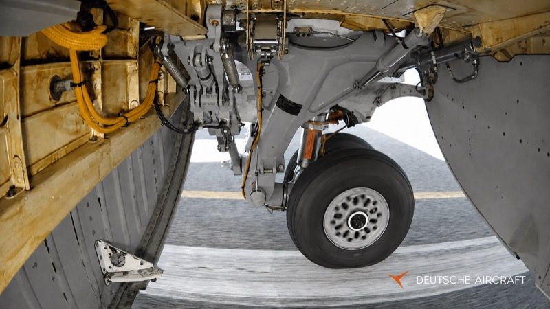 Close-up of a D328 main landing gear leg and wheel in its bay, showing the oleo strut, hydraulic lines and structural mountings