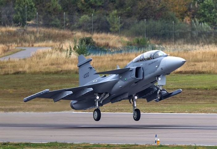 A grey two-seat Saab Gripen fighter with its landing gear extended, flying low over a runway with the number 4000 on its tail fin